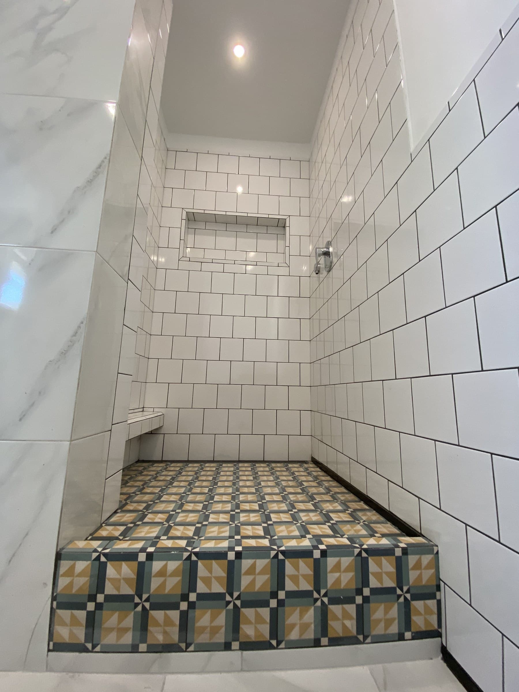 Finished walk-in shower by Kuzbyt Construction, tiled in white square tile with a recessed niche and a patterned tiled floor