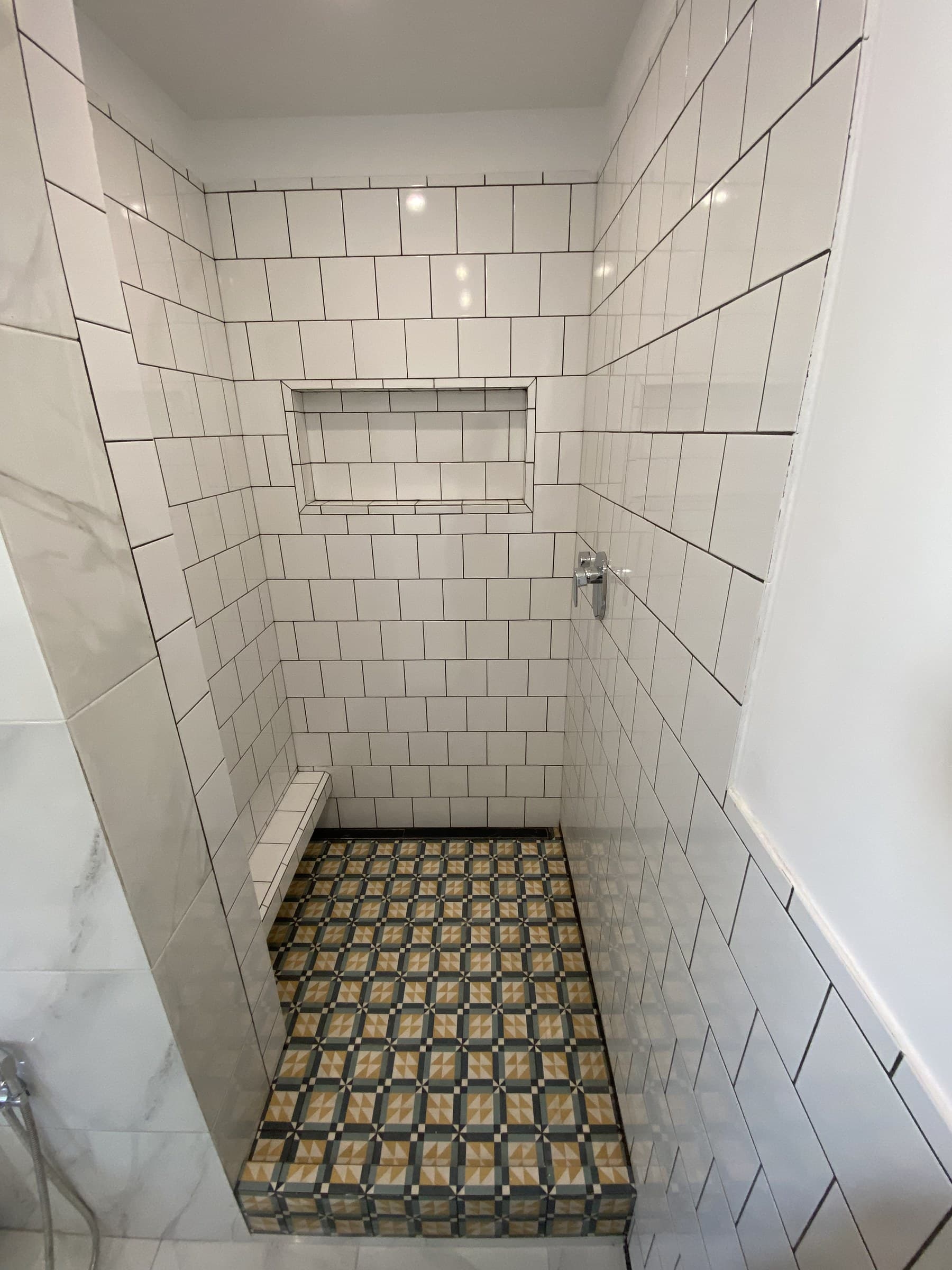 Walk-in shower lined in white square tile with a recessed niche above a patterned tiled floor