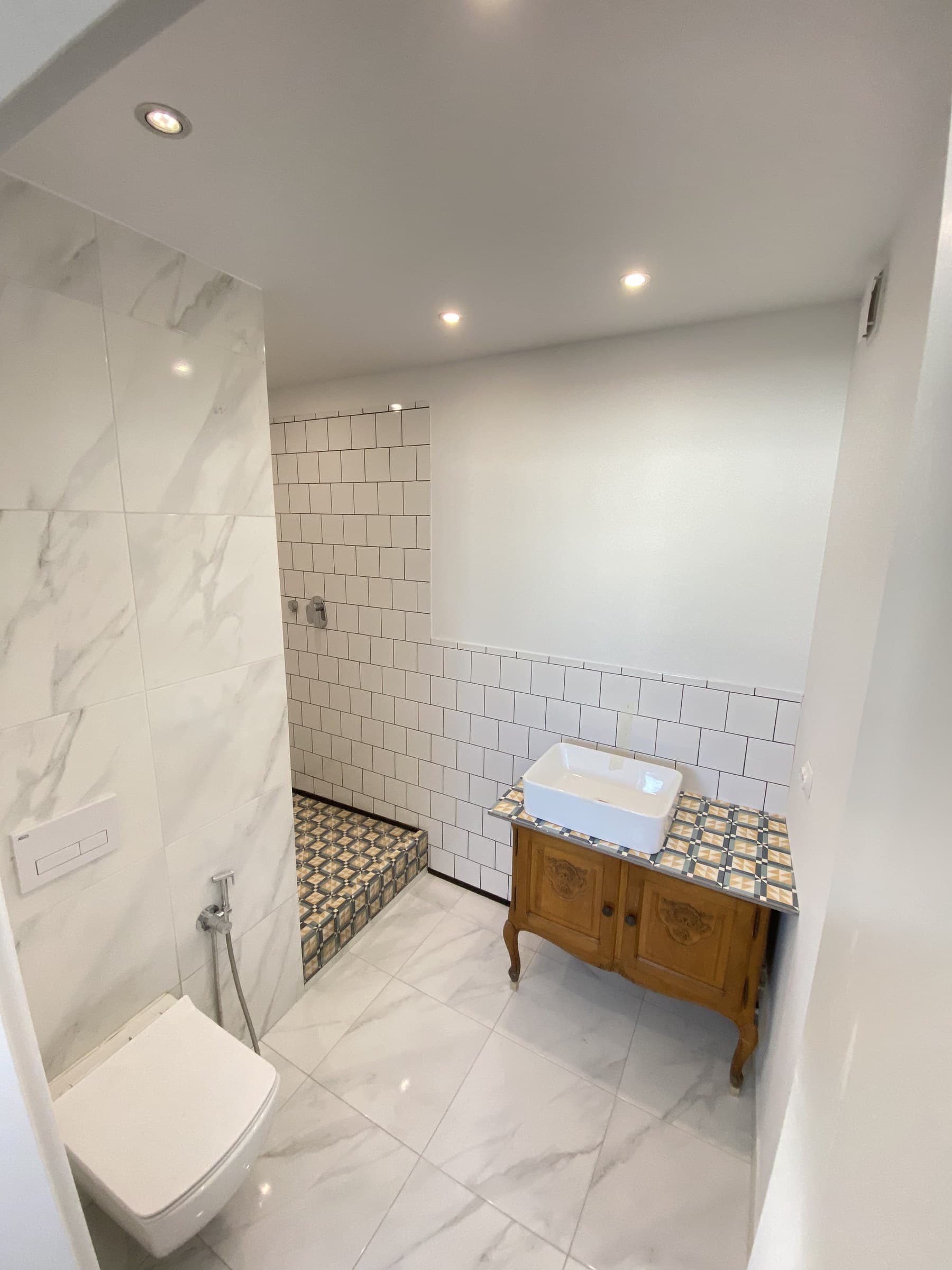 Bathroom with white tiled walls, a wall-hung toilet, a timber vanity and a patterned tiled floor area