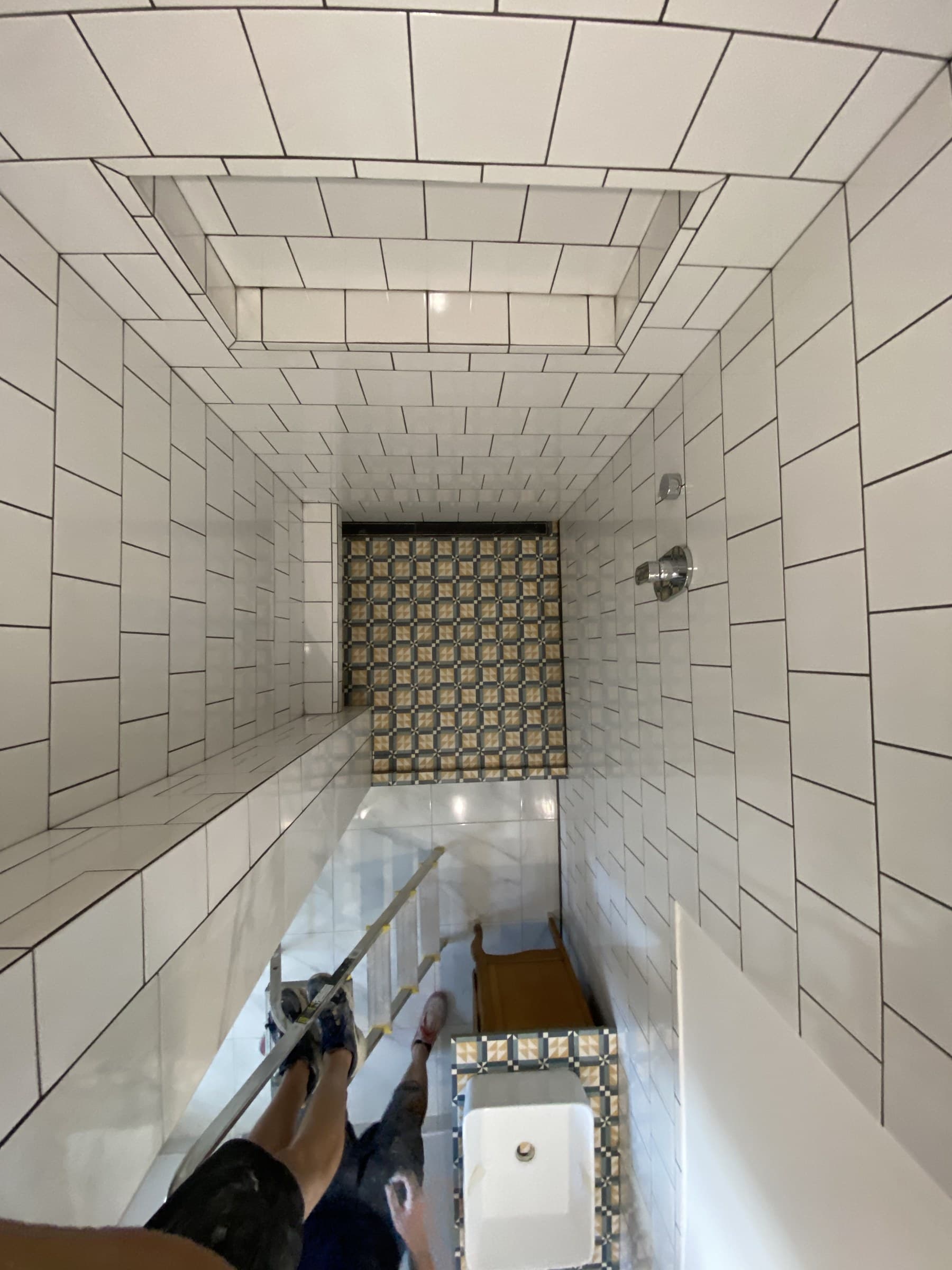 Long view of the white-tiled bathroom during tiling, showing the patterned floor and tiled ceiling detail