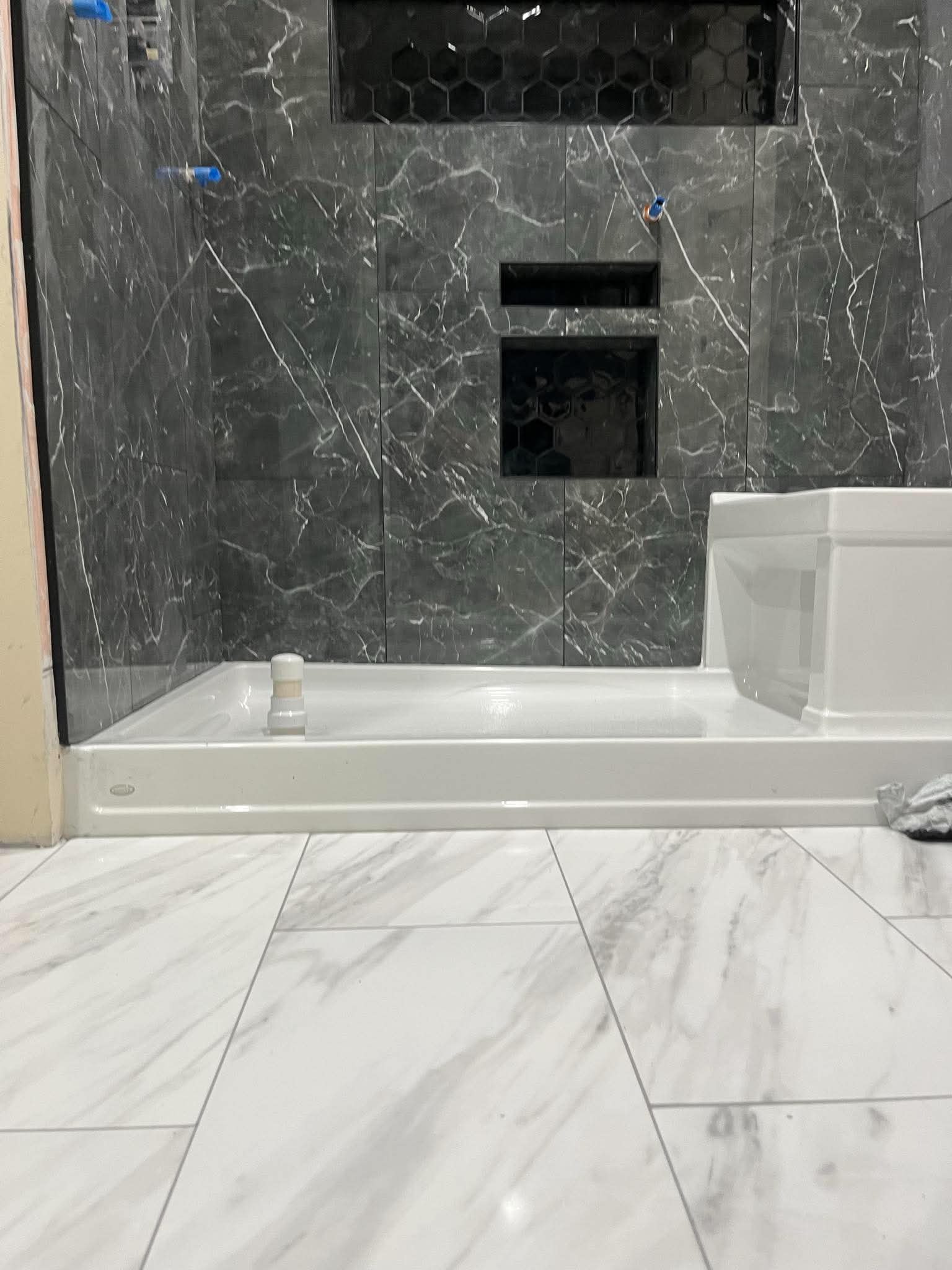 Shower surround in dark stone-look tile with a recessed hexagon-mosaic niche above a white shower tray