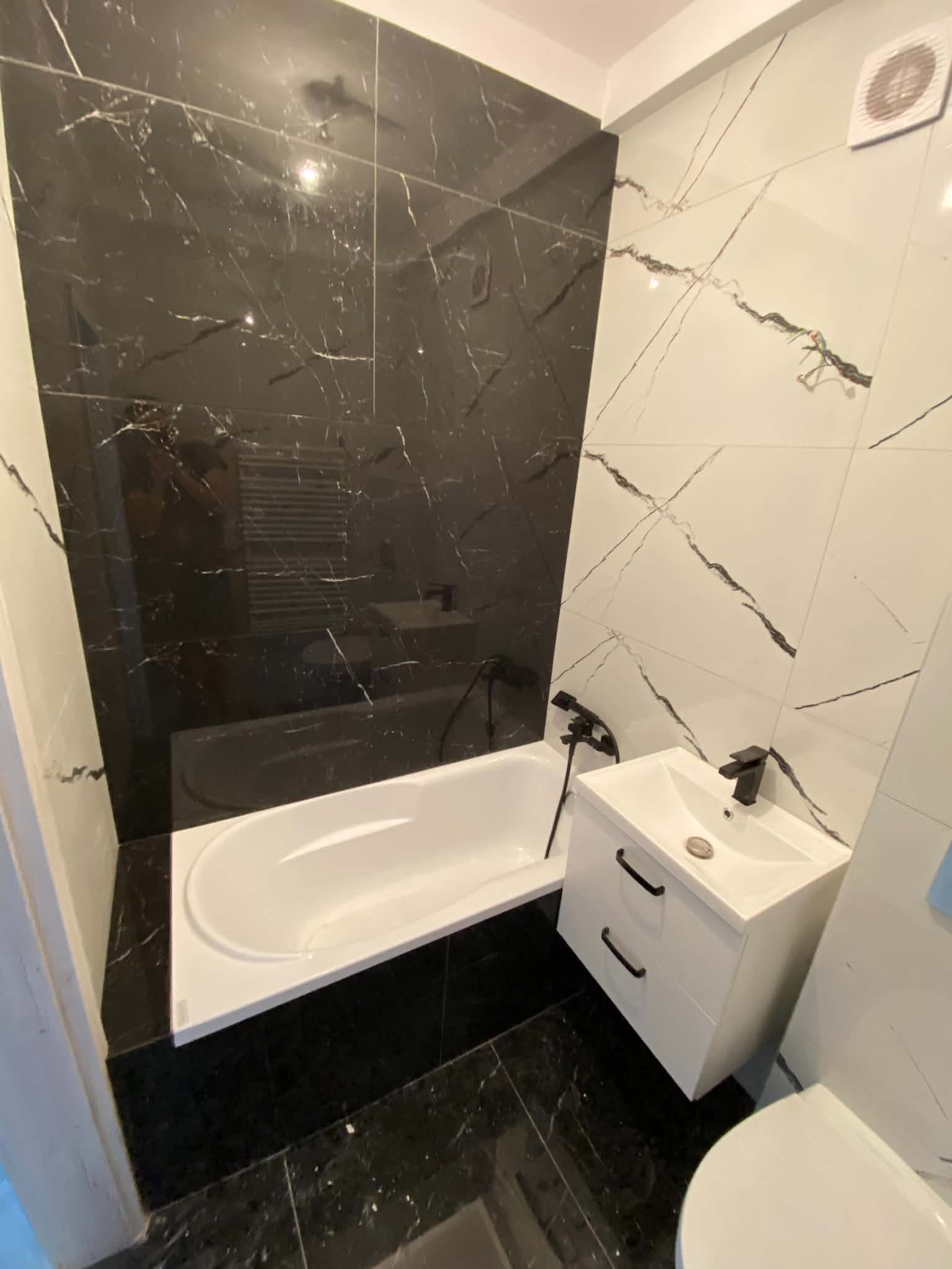 Bathroom with a dark marble-look feature wall behind a white bath, a wall-hung vanity and a dark tiled floor