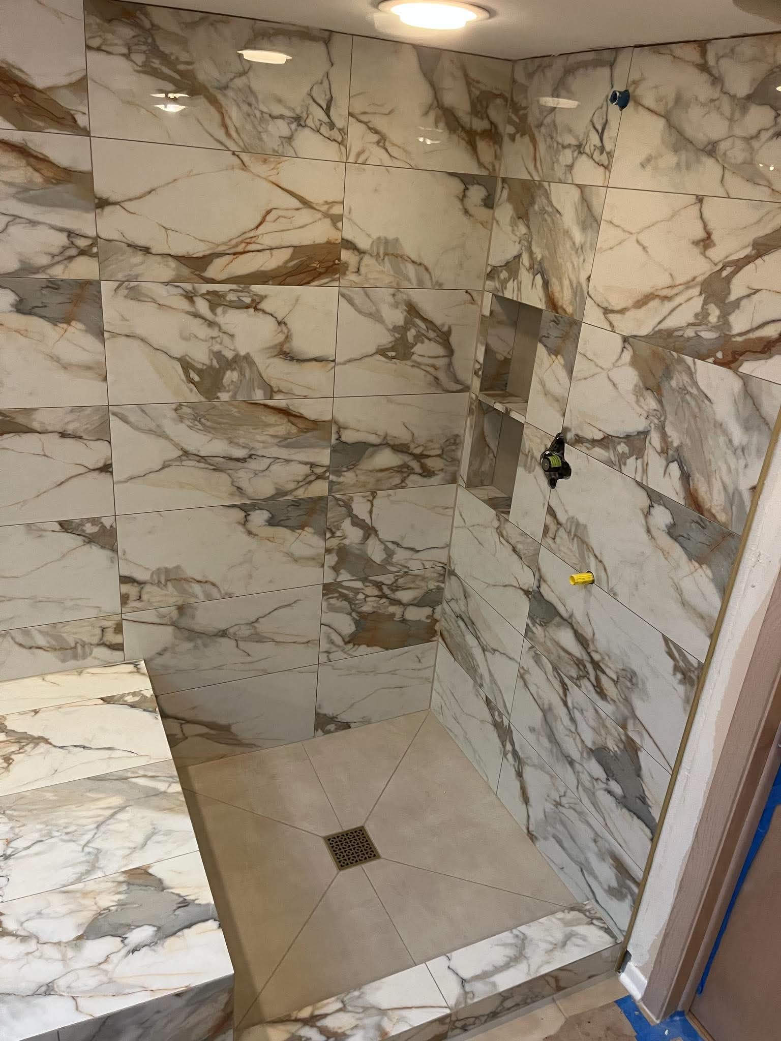 Walk-in shower lined in heavily veined cream and grey marble-look porcelain with a level-entry tiled floor