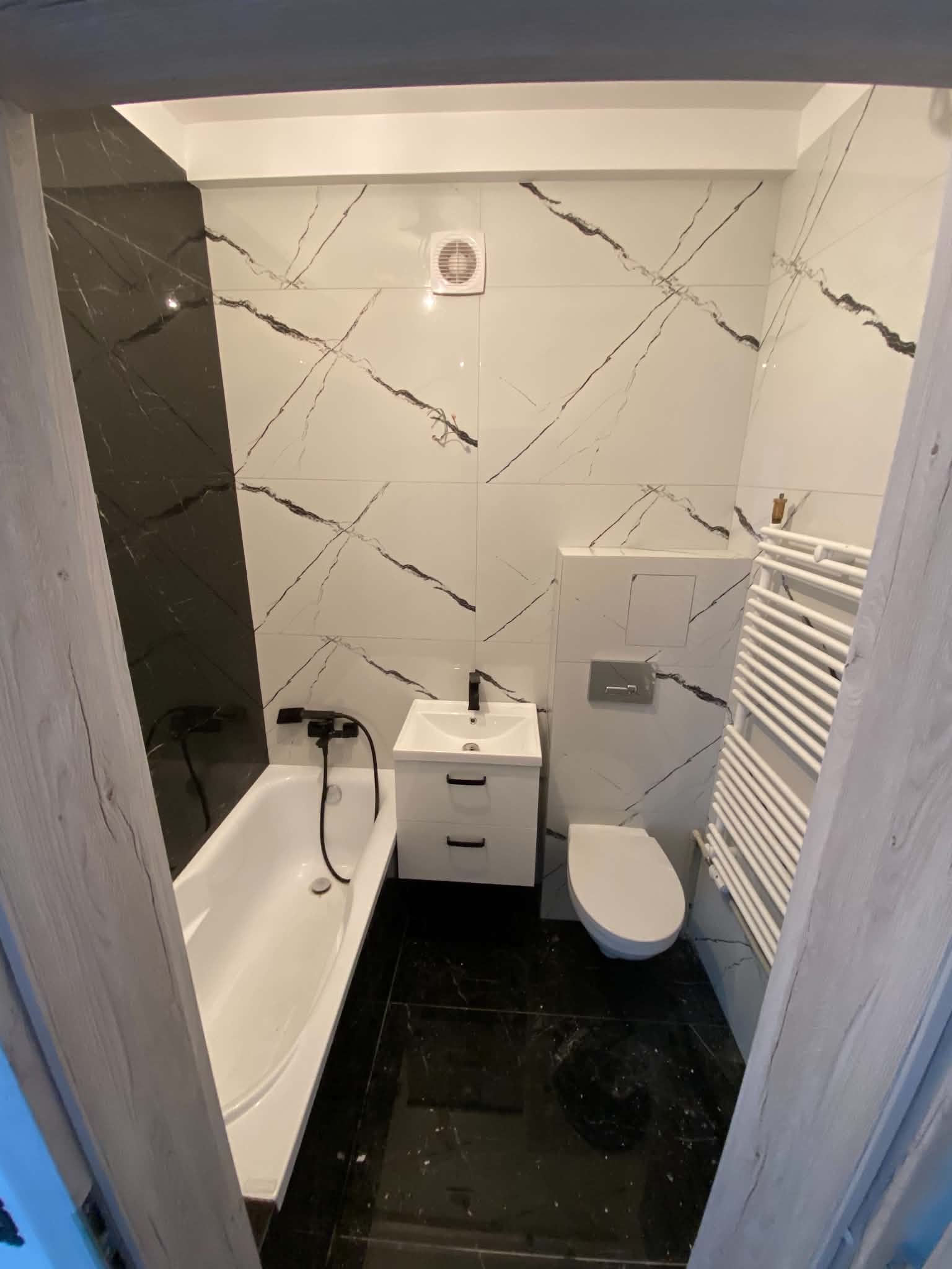 Bath set beneath a dark tiled recess with white marble-look walls and a dark floor