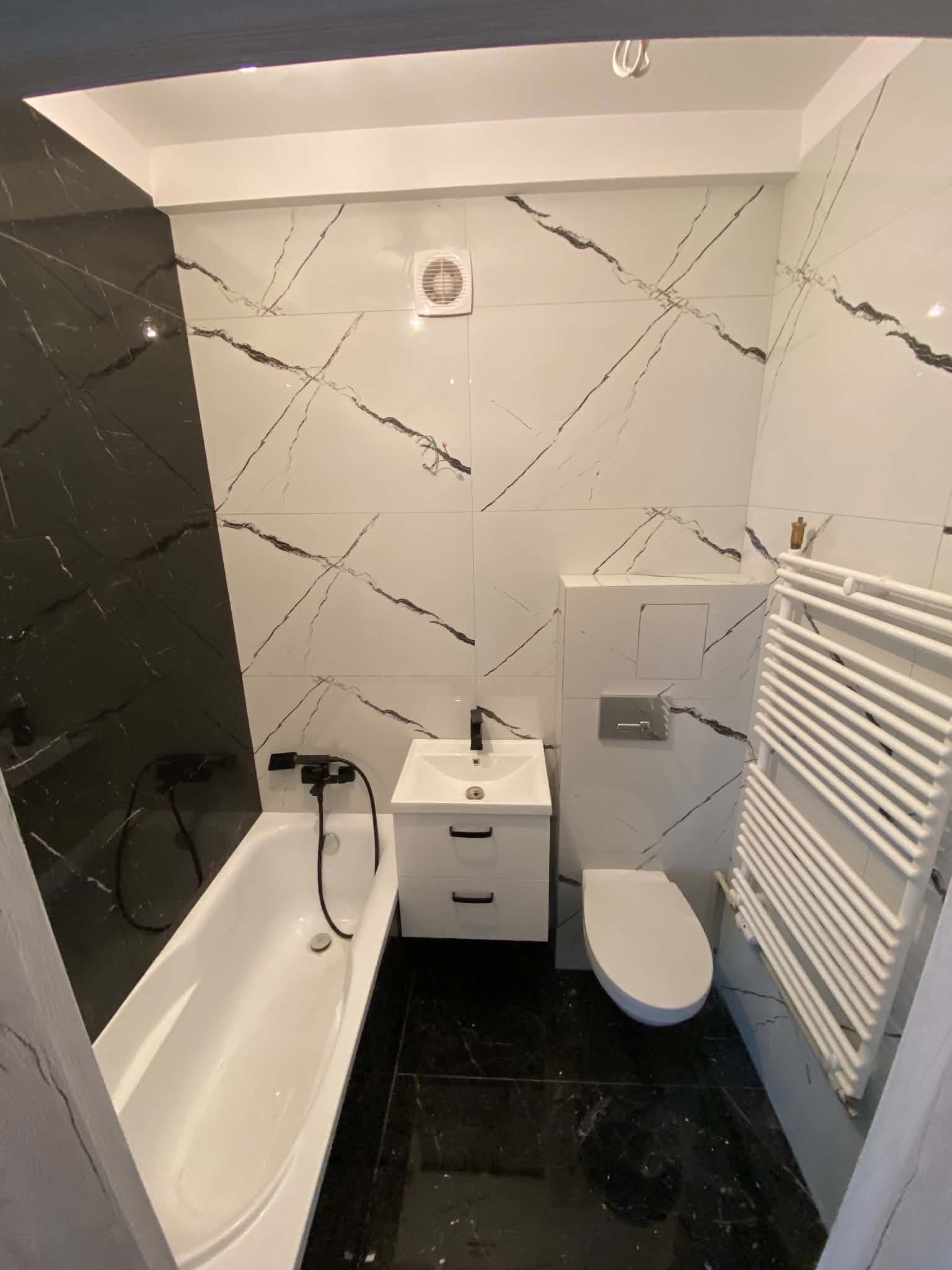 Bathroom corner showing the bath, vanity, toilet and white ladder radiator against marble-look tile