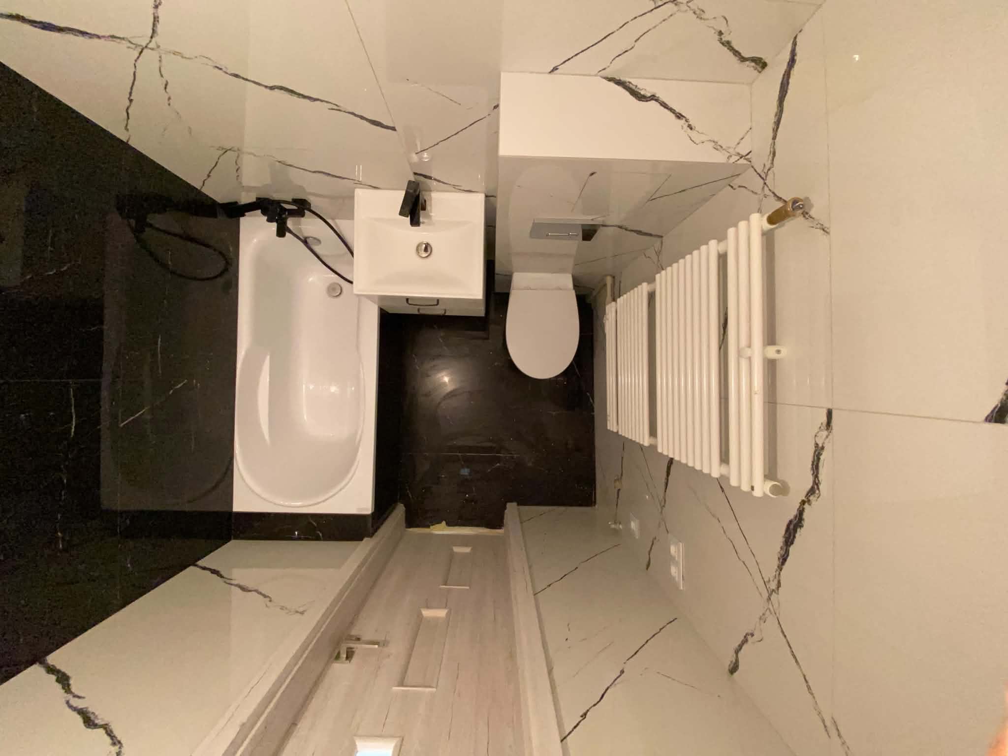Wide view along the finished marble-look bathroom toward the bath and radiator